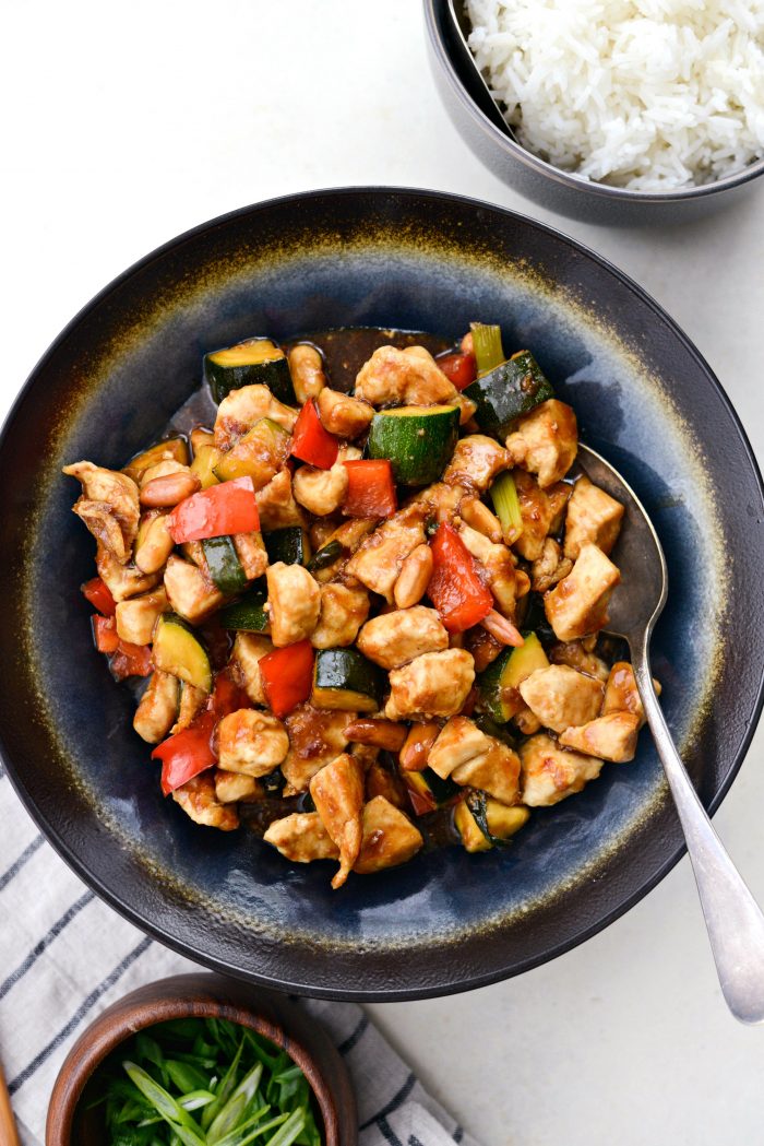 blue and black serving dish with kung pow chicken with a bowl of rice and green onions