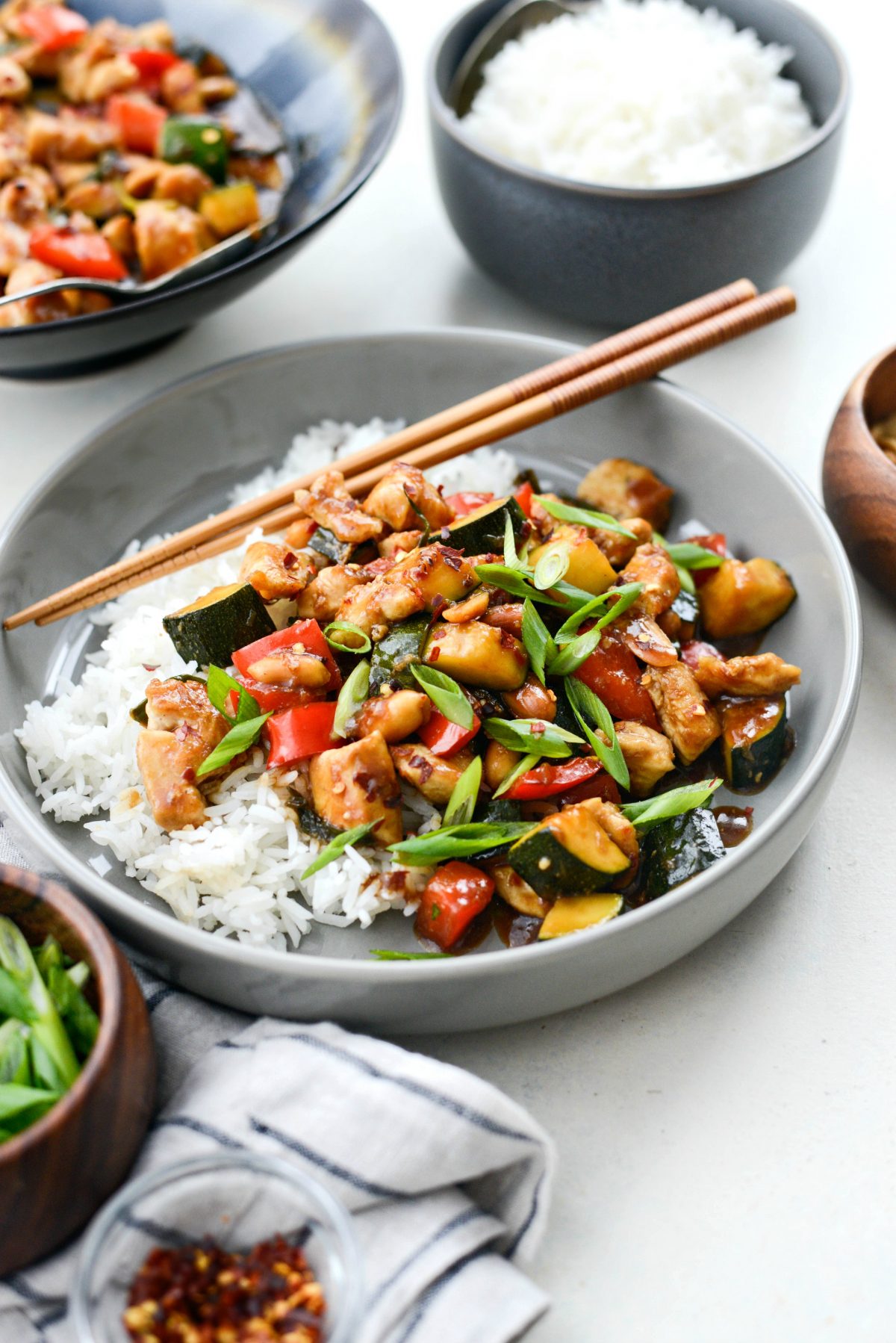 Kung Pao Chicken Stir-fry in grey bowl with rice, green onions and chopsticks.