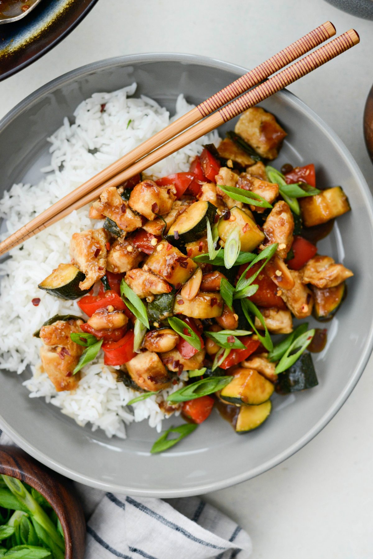 close up of Kung Pao Chicken Stir-fry in grey bowl with chopsticks.