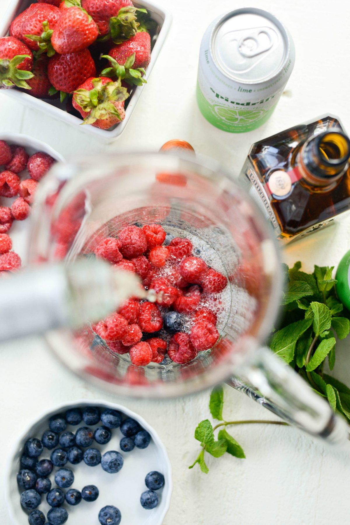 pouring bottle of wine into glass pitcher with berries.