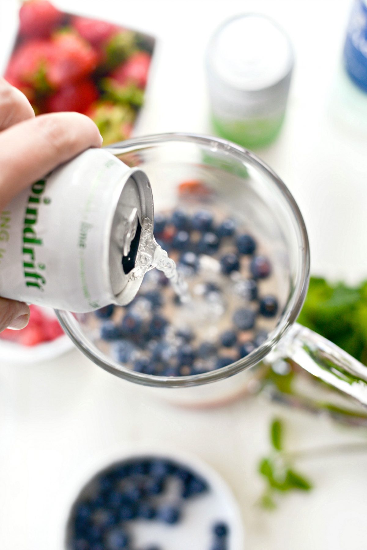 pouring in sparkling lime water into pitcher with wine, cointreau and berries.