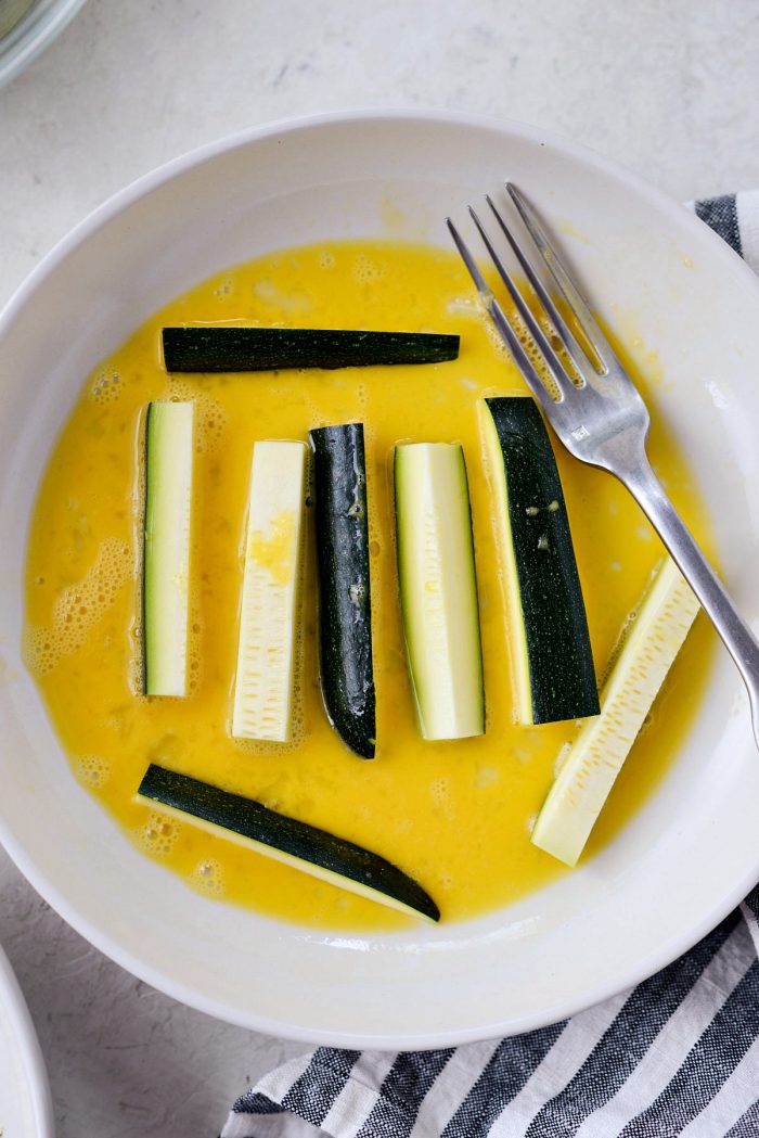 zucchini fries in shallow bowl of beaten egg