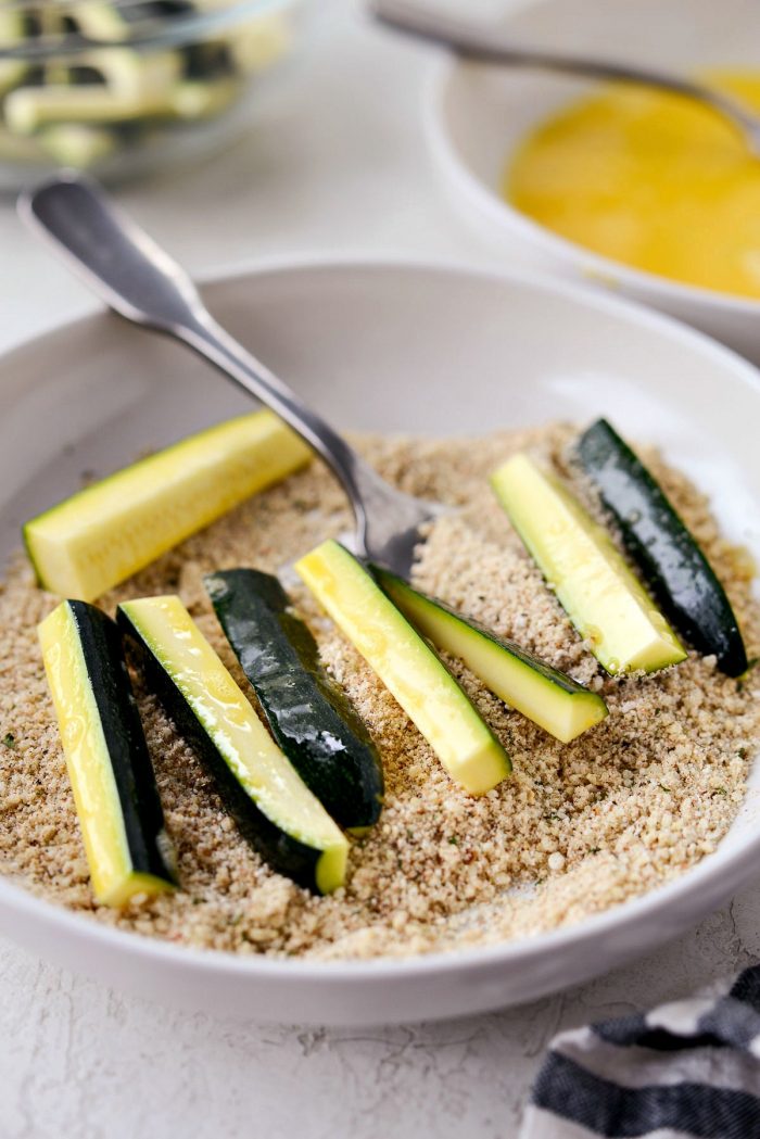 zucchini in shallow bowl of parmesan breadcrumb mixture.