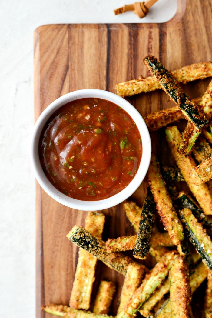 Close up of basil ketchup in grey bowl on wood cutting board with zucchini fries.