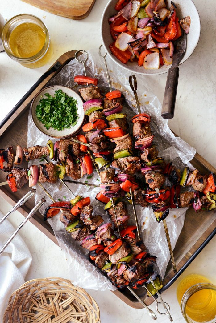grilled marinated steak kebabs on wooden tray with glasses of beer.