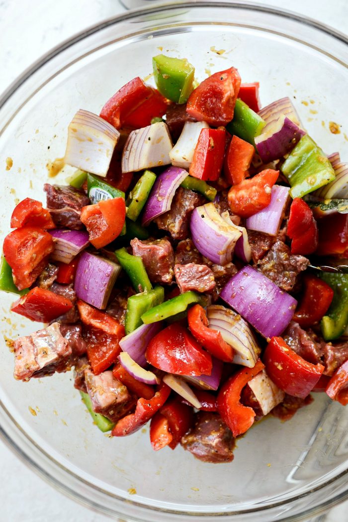 steak and vegetables tossed with marinade in glass bowl.