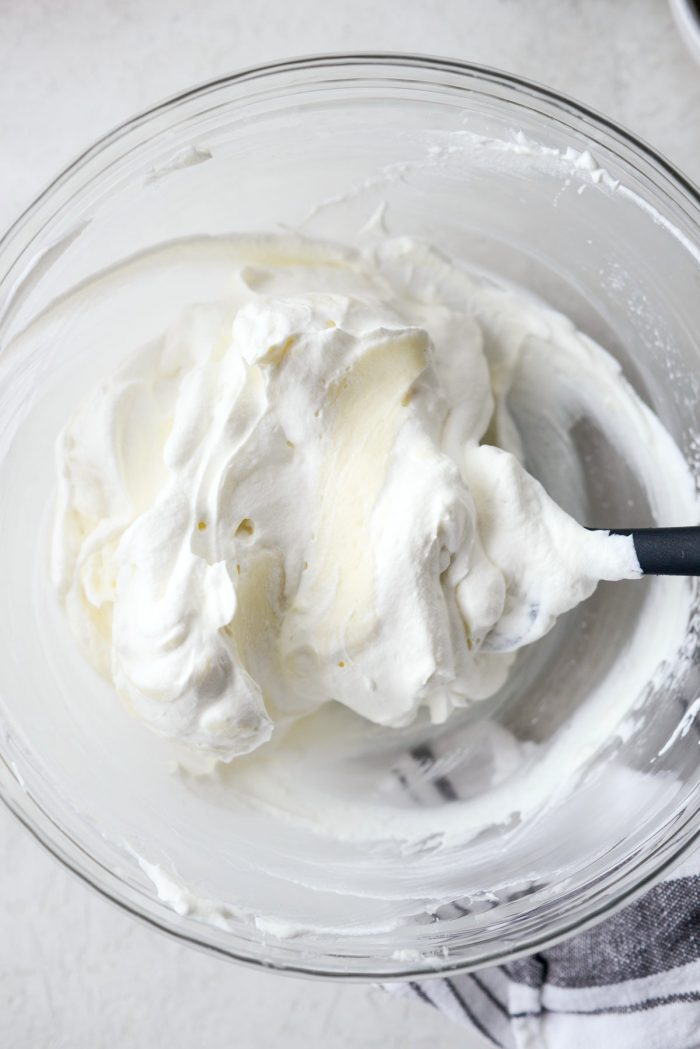 whipped cream is being folded into cream cheese mixture with rubber spatula.