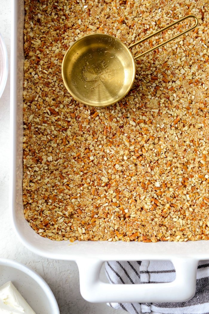 crust mixture pressed into white pan with gold measuring cup