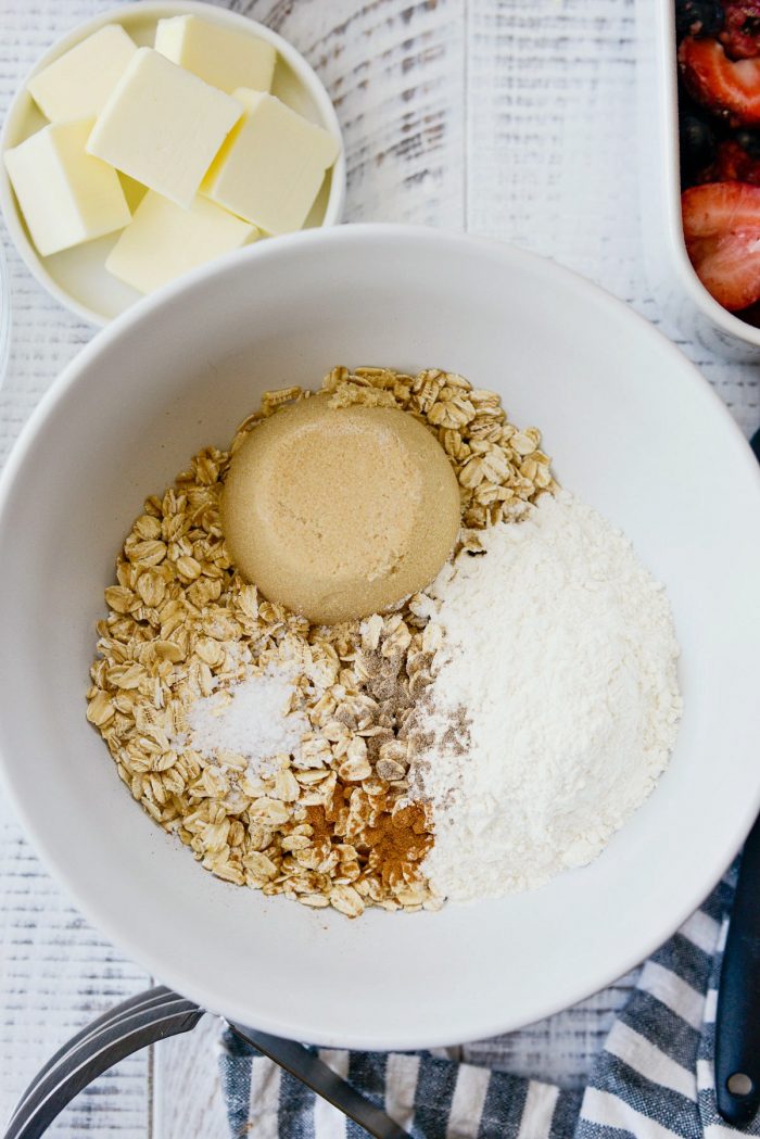 Oats, sugar, flour, salt, cardamom and cinnamon in white bowl.