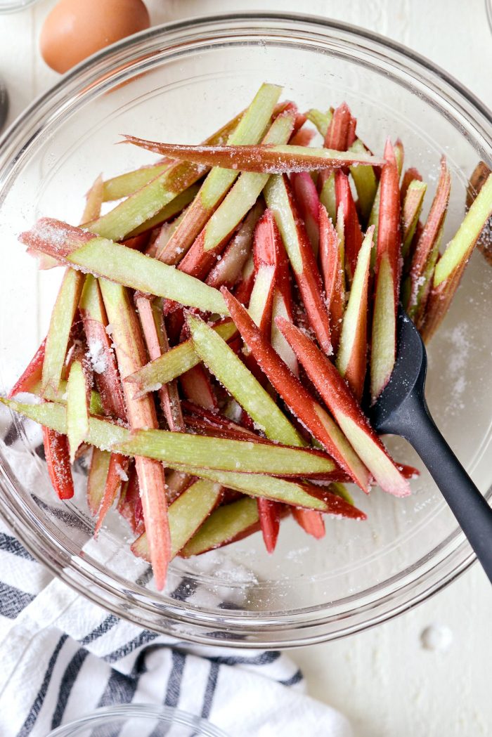 sliced rhubarb tossed with sugar in clear bowl.
