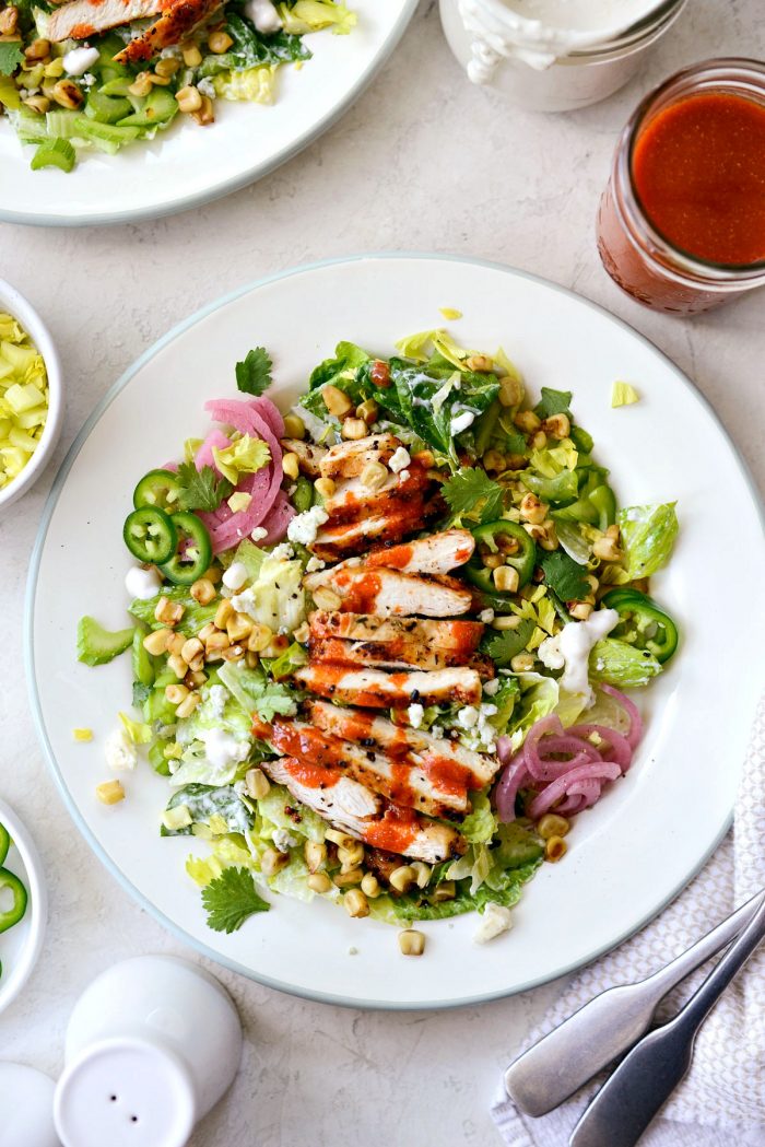 buffalo grilled chicken salad is served on white plates with light blue edge.