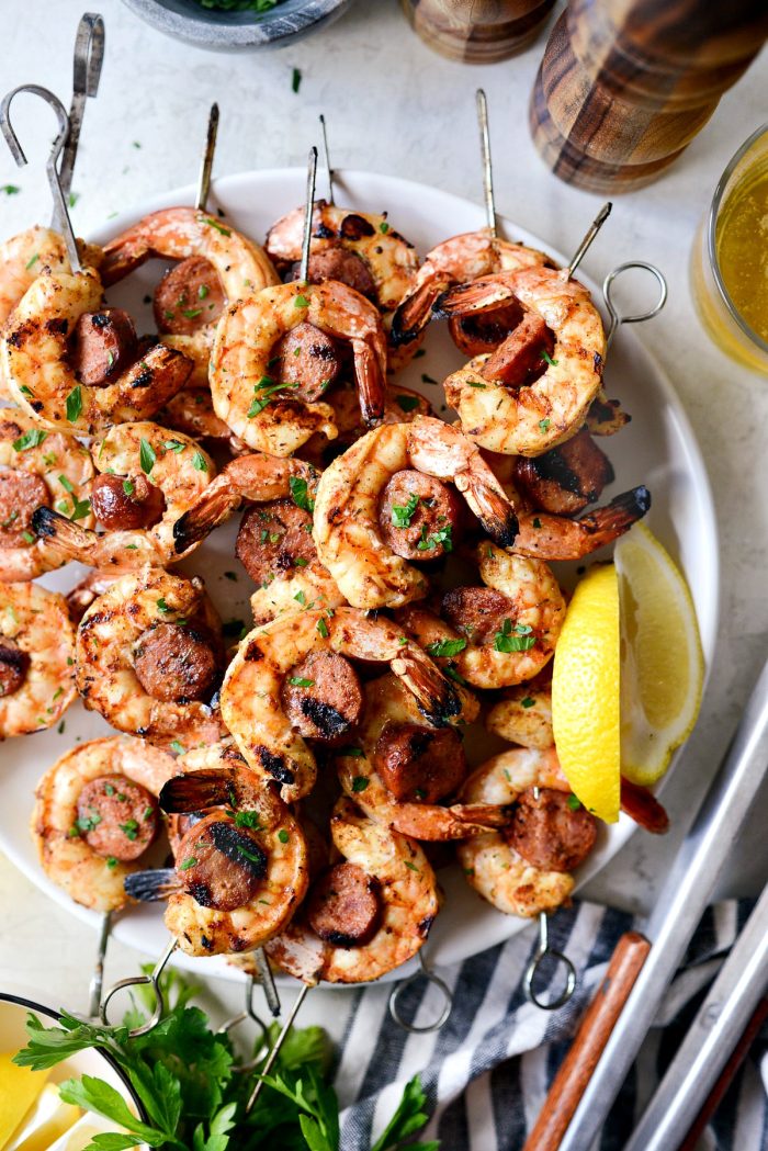 Grilled Cajun Shrimp and Andouille Skewers on white plate with lemon wedges.