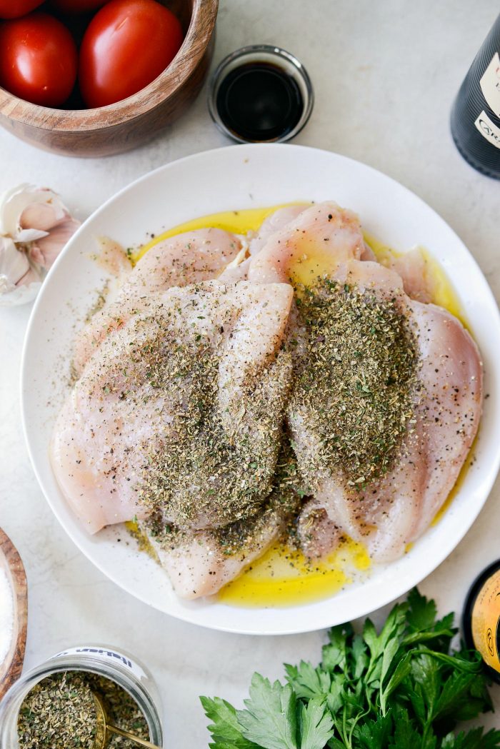 thinly pounded chicken on white plate with italian seasoning, lemon juice, olive oil, s & p