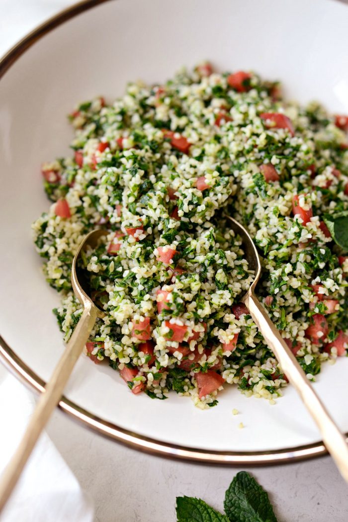 two gold spoons serving homemade tabbouleh from a cream bowl with gold edge.