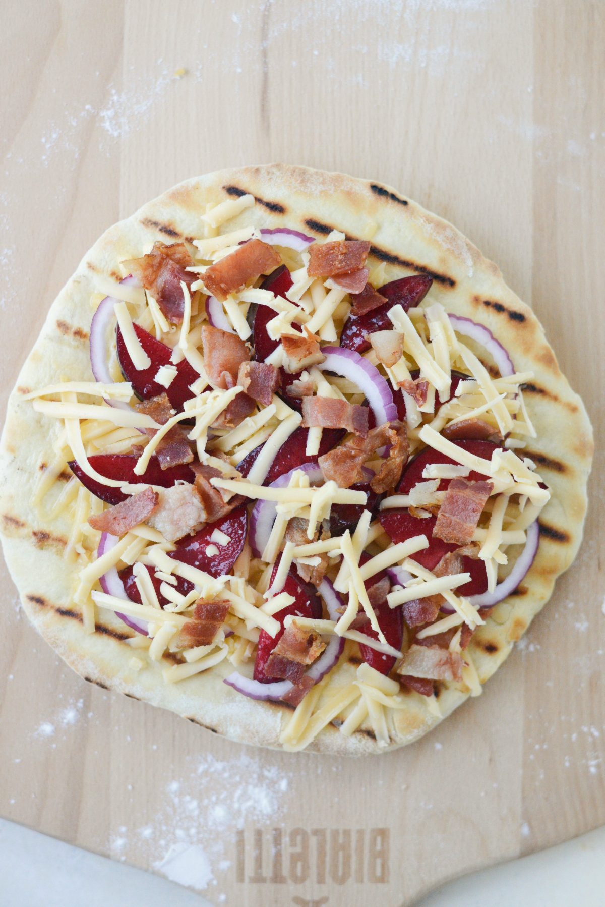 grilled pizza dough topped with red onion, plums, bacon and more gouda.