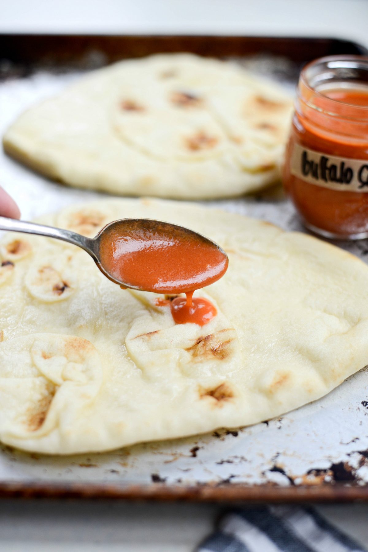 spreading spoonfuls of buffalo sauce on the naan.
