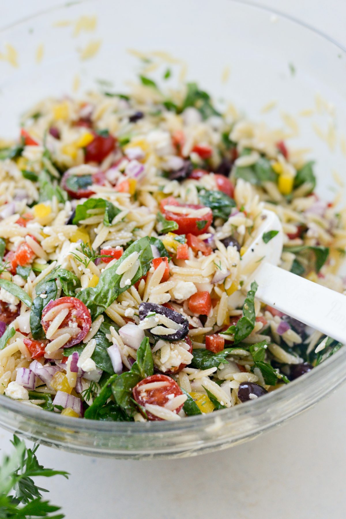 Tossing the Greek Orzo Salad with a white rubber spatula.