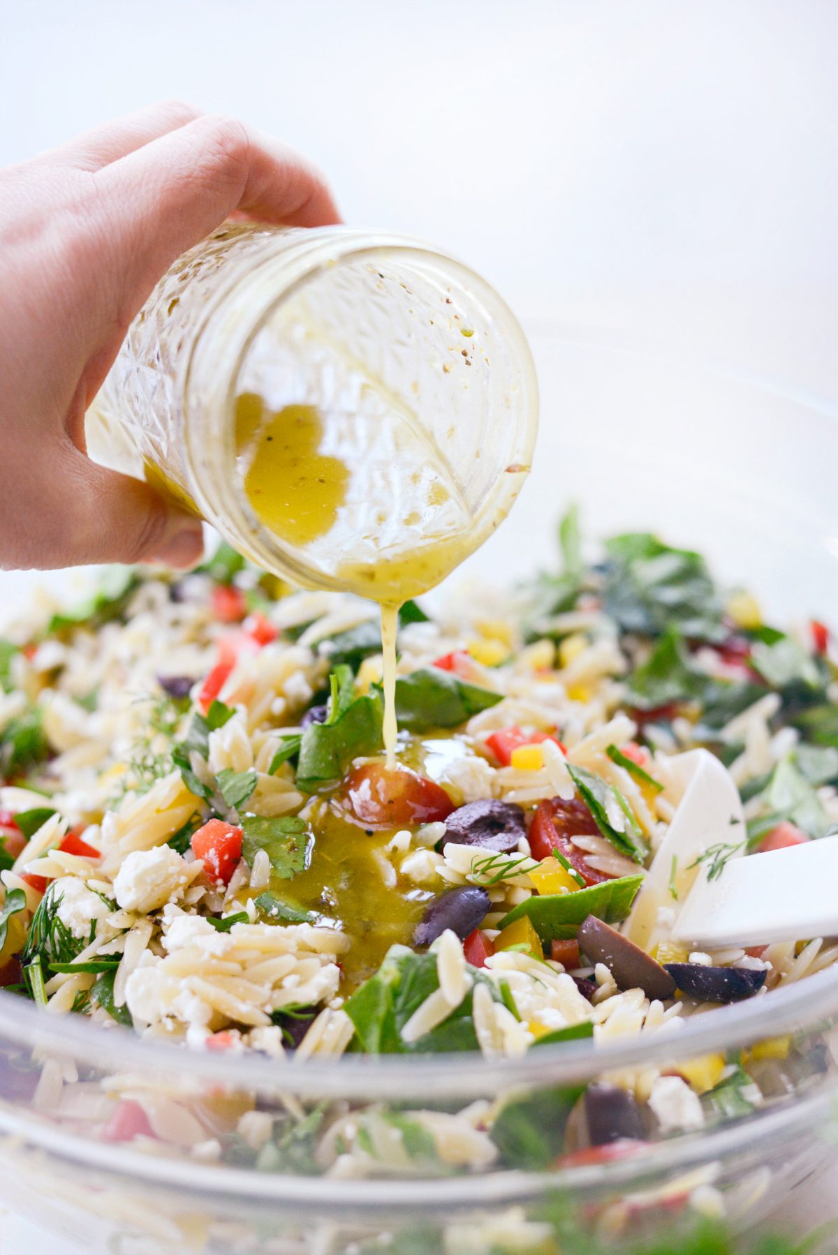 Pouring homemade Greek Salad Dressing onto salad.