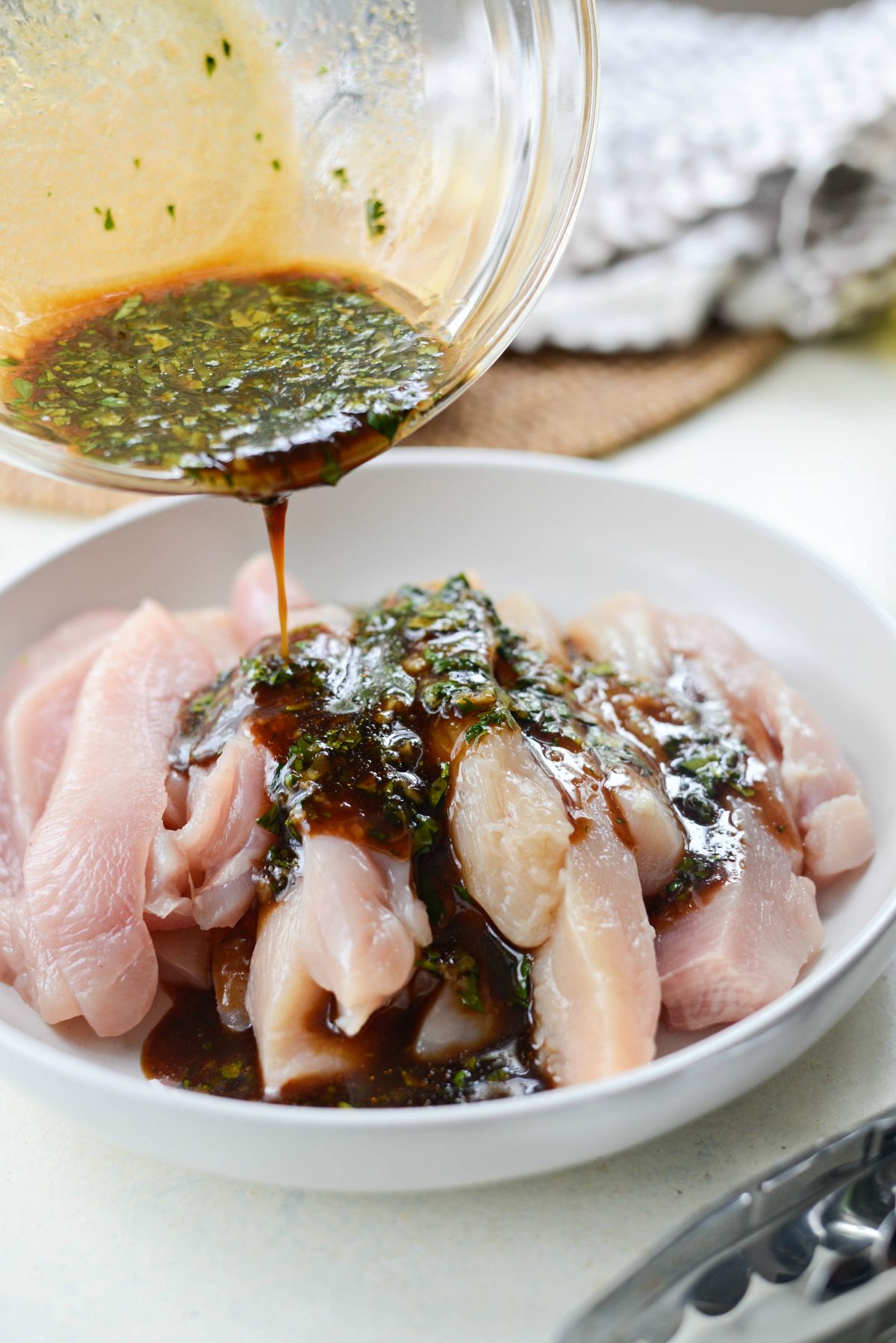 pouring marinade over strips of chicken