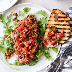 white plate with arugula, grilled chicken bruschetta and grilled bread