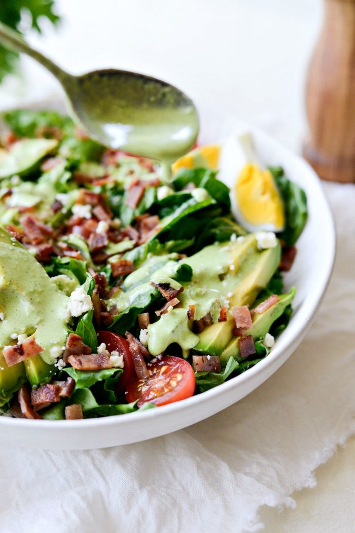 drizzling greek yogurt Green Goddess salad dressing on cobb salad.