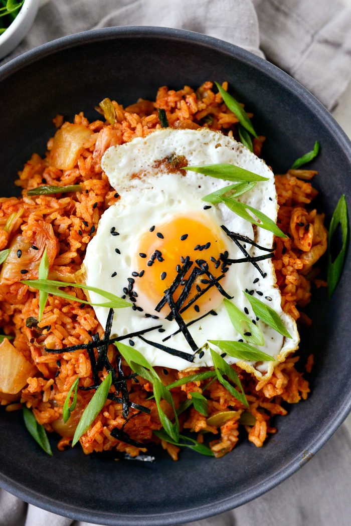 kimchi fried rice in black bowl with fried egg, black sesame seeds, green onion and nori