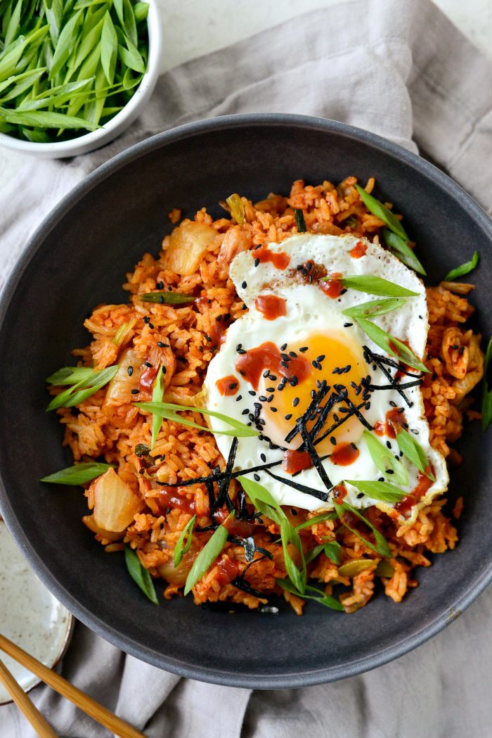 kimchi fried rice in black bowl with toppings and gochujang hot sauce.