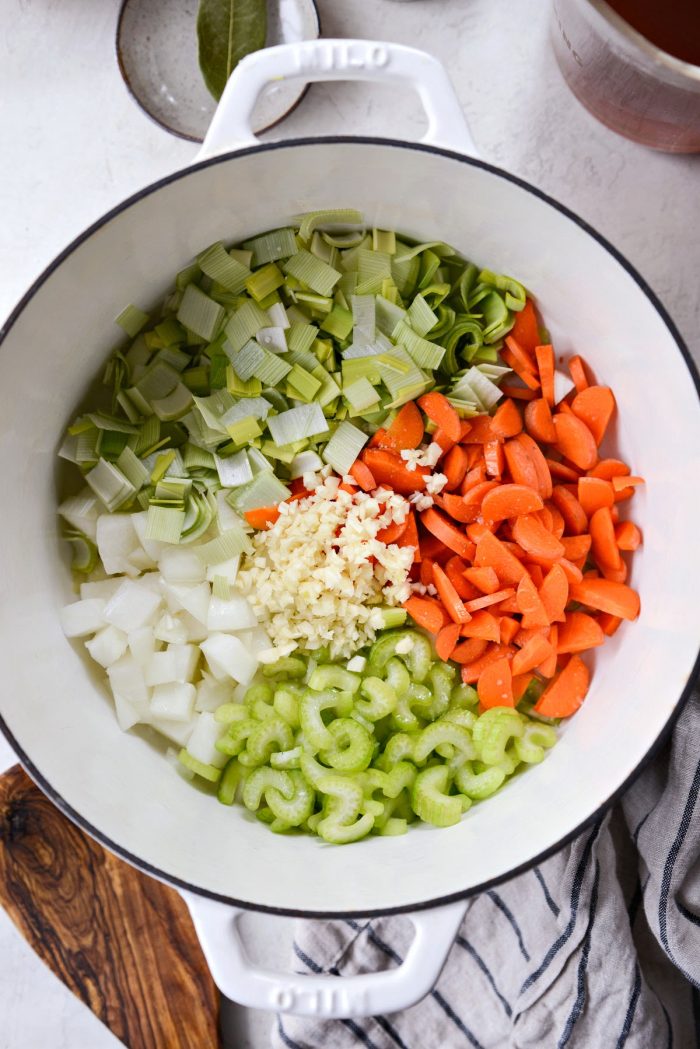 white dutch oven with onions, leeks, carrots, celery and garlic.