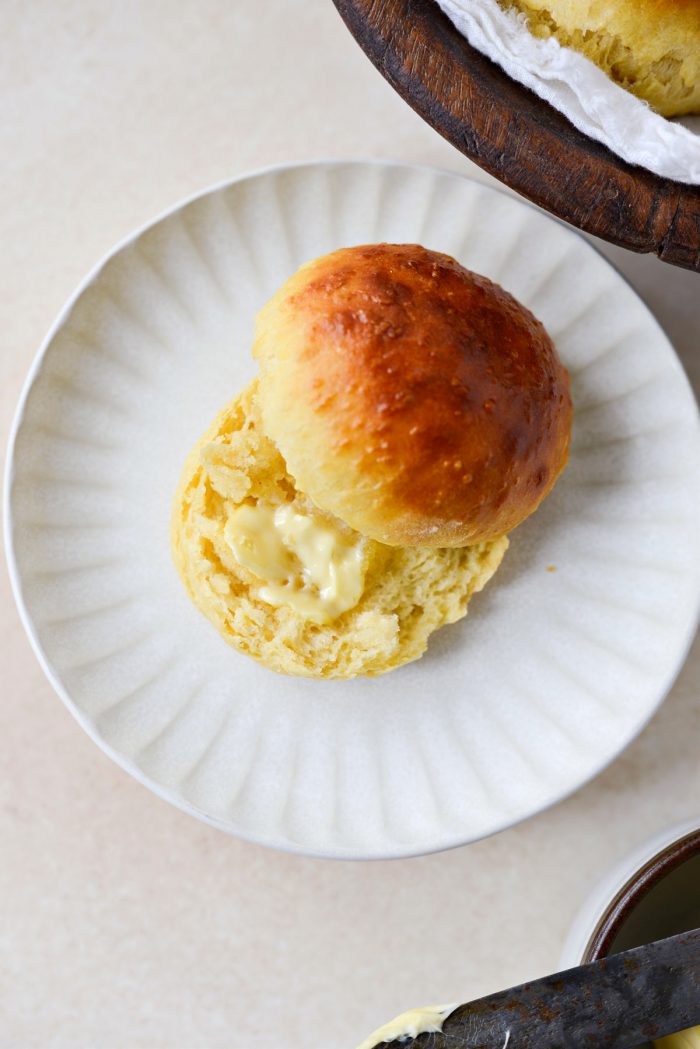 Brioche Dinner Rolls in half with butter on a cream plate.