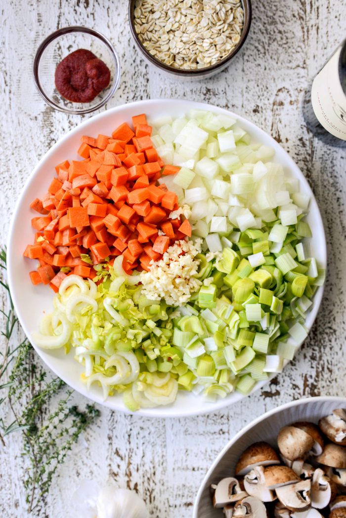 diced carrot onion, leek, celery and garlic on a white plate.