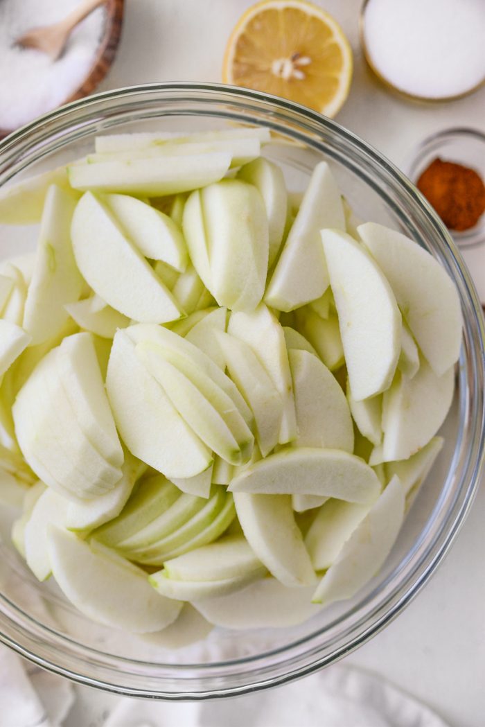 peeled and sliced granny smith apples in a glass bowl.