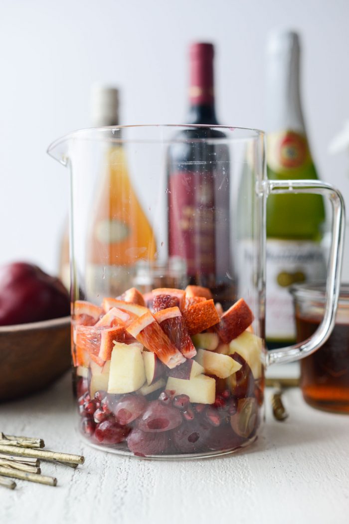 grapes, pomegranate arils, apples and blood oranges in a glass pitcher.