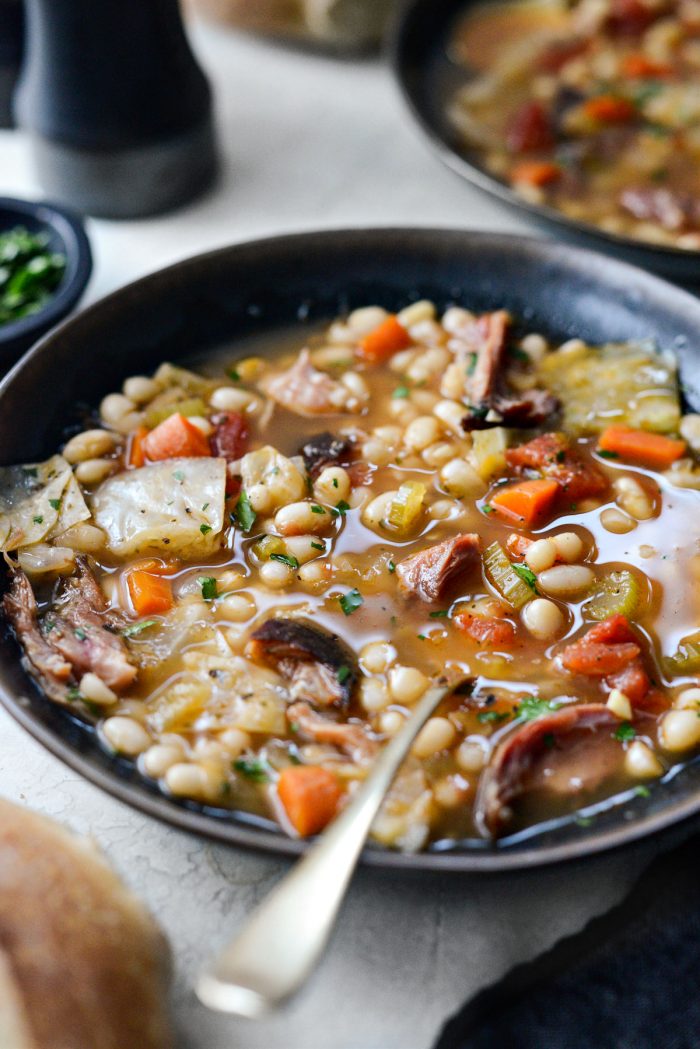 Rustic Ham and Bean Soup in black and gold bowl with gold spoon.