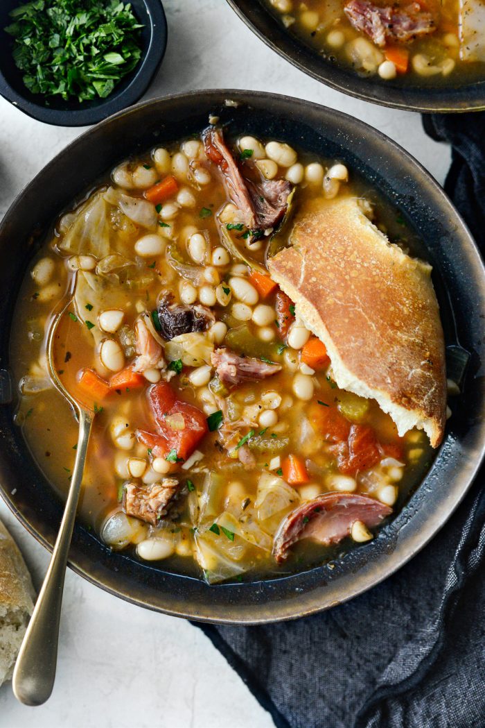 A hunk of crusty sourdough in a bowl of Rustic Ham and Bean Soup.