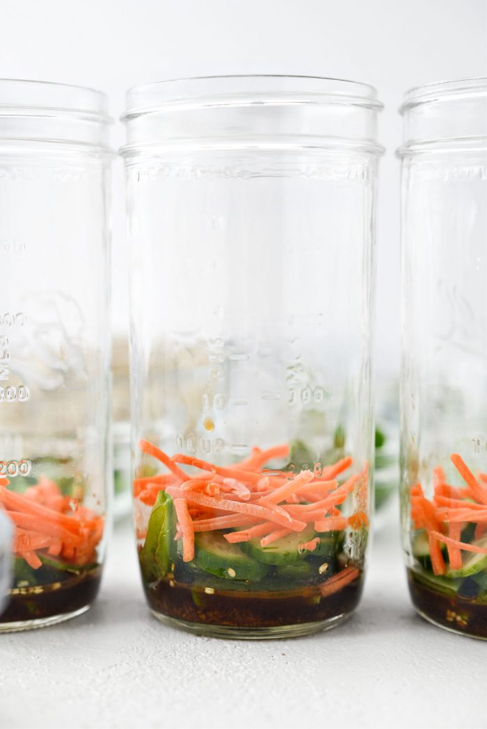 mason jar with dressing, snap peas, cucumber and carrots.