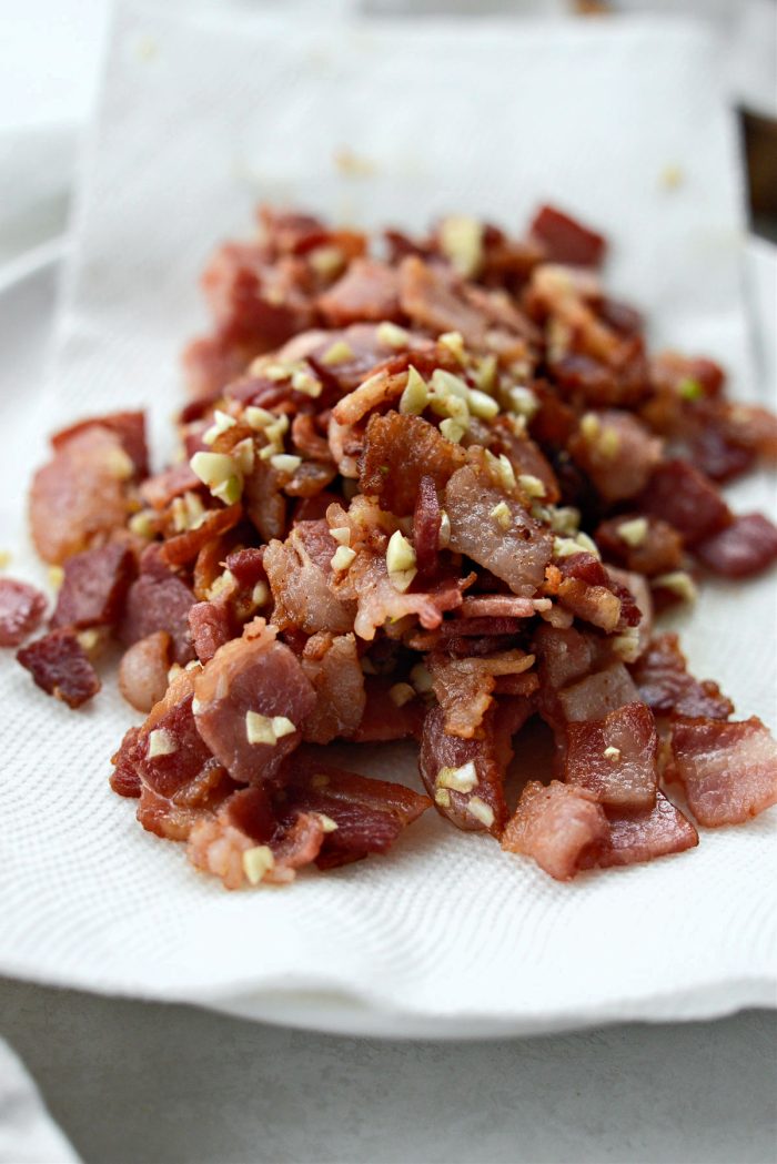 Crispy bacon and cooked garlic on a paper towel-lined plate.